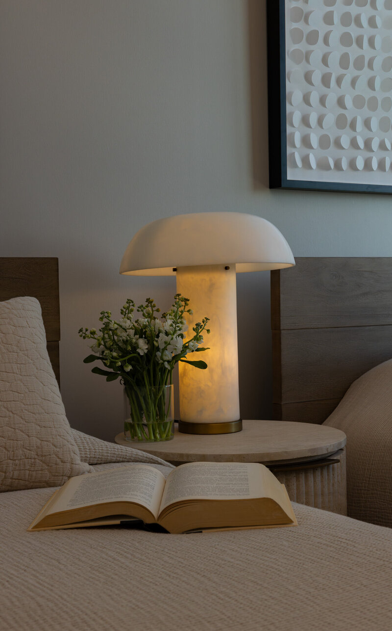Detail of a secondary bedroom featuring warm wood bedframes, textured bedding, a fluted travertine nightstand with flowers and a book, designed by Sister Studio.