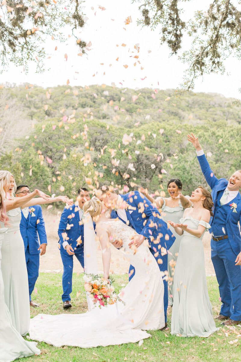 Group of bridesmaids and groomsmen shower The Mateis with rose petals to celebrate their union after the wedding ceremony