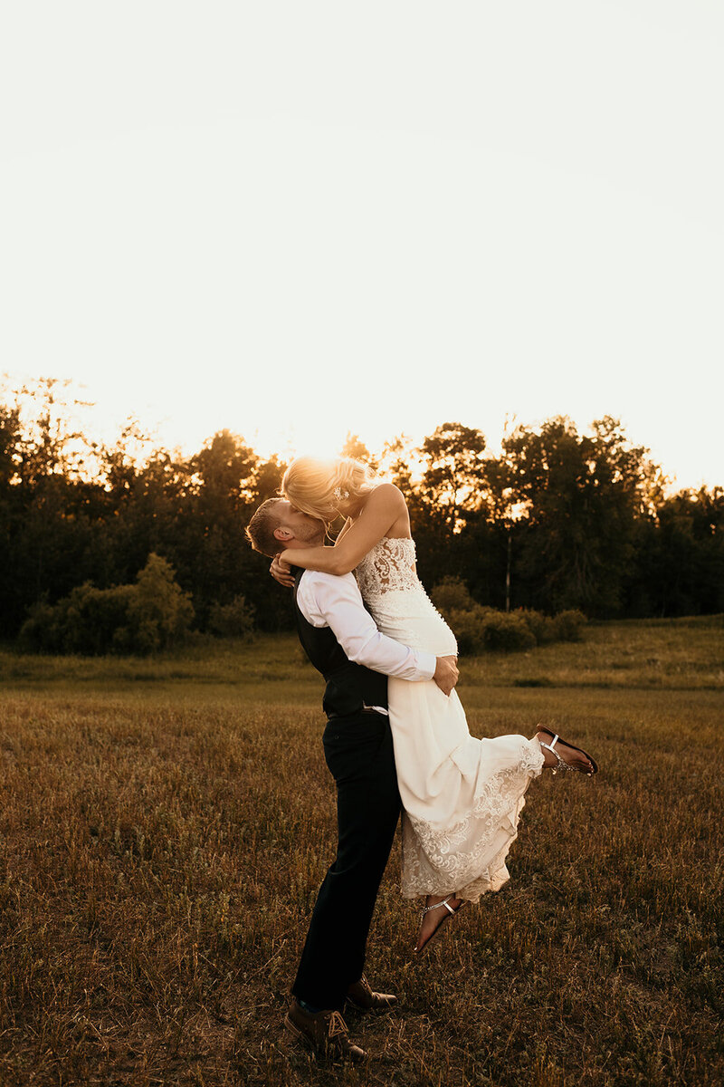 groom holding up bride in sunset field