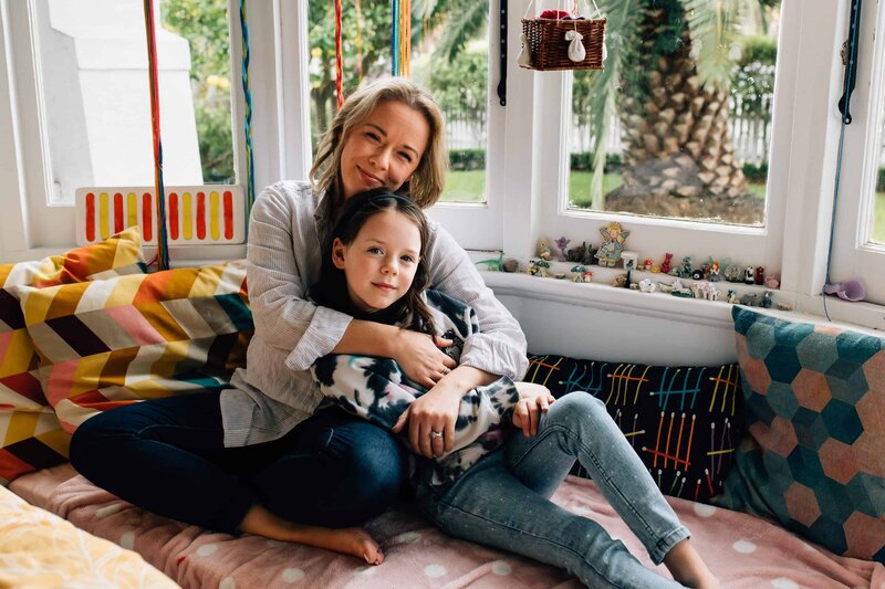 Mother with arms around daughter, sitting in window seat during in home family photoshoot by And So I Don't Forget Photography Melbourne