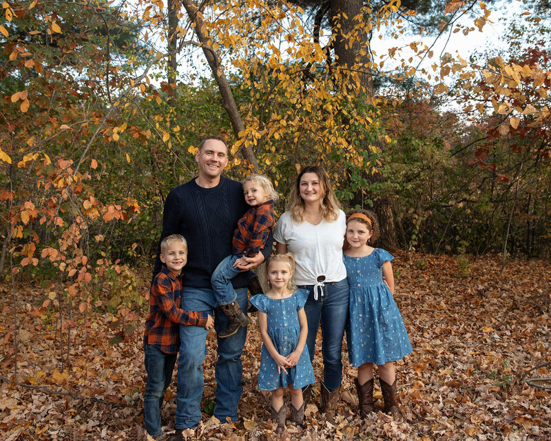 Fall family picture of 6. Dad, Mom, 2 boys and 2 girls. Lot of fall colors in the background.