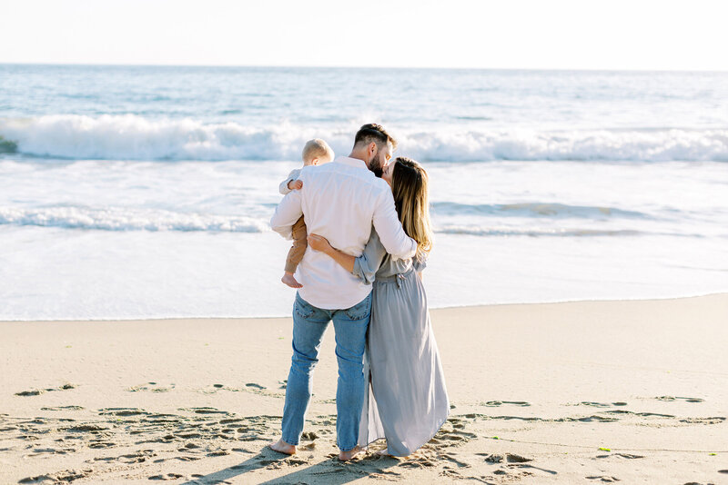 A mom and dad kiss on the beach during their family photos in Santa Barbara