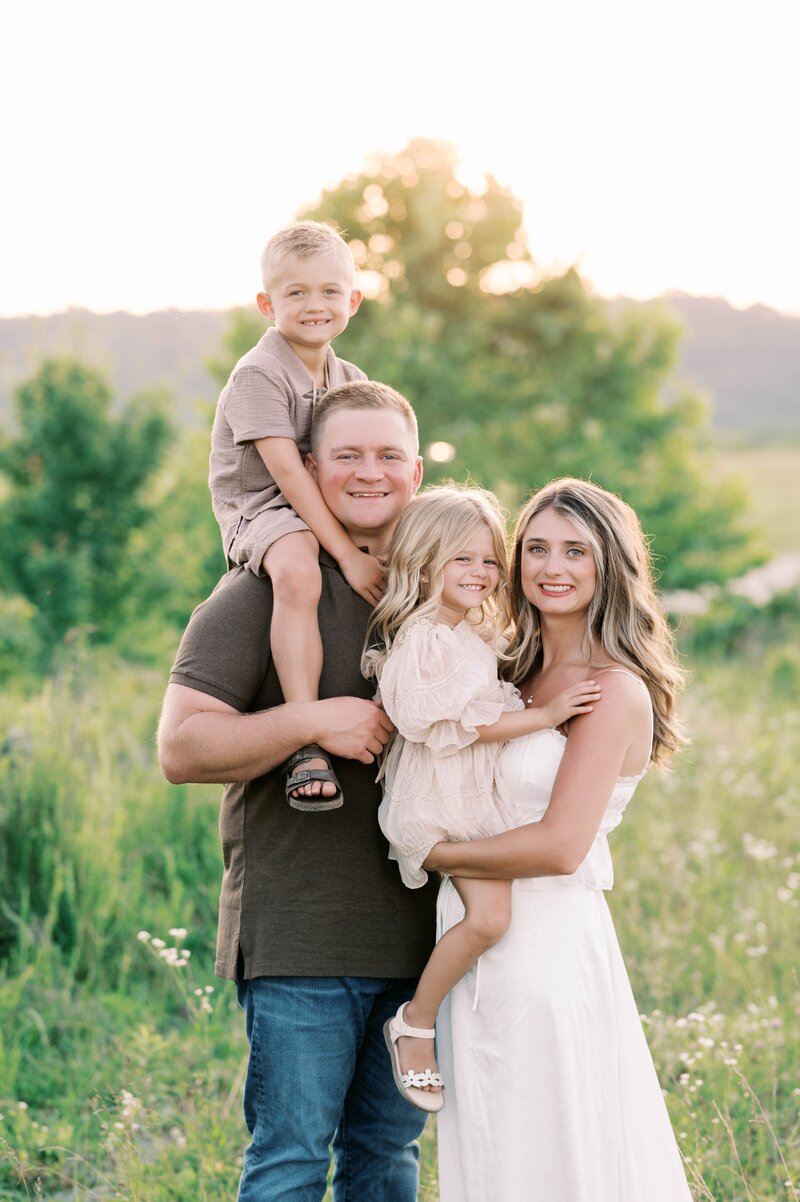 Family of four posing in front of green grass and trees