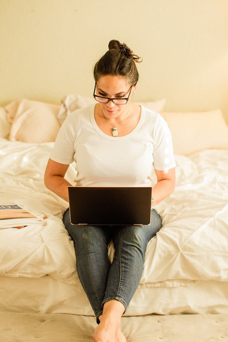 women sitting on a bed working on her computer