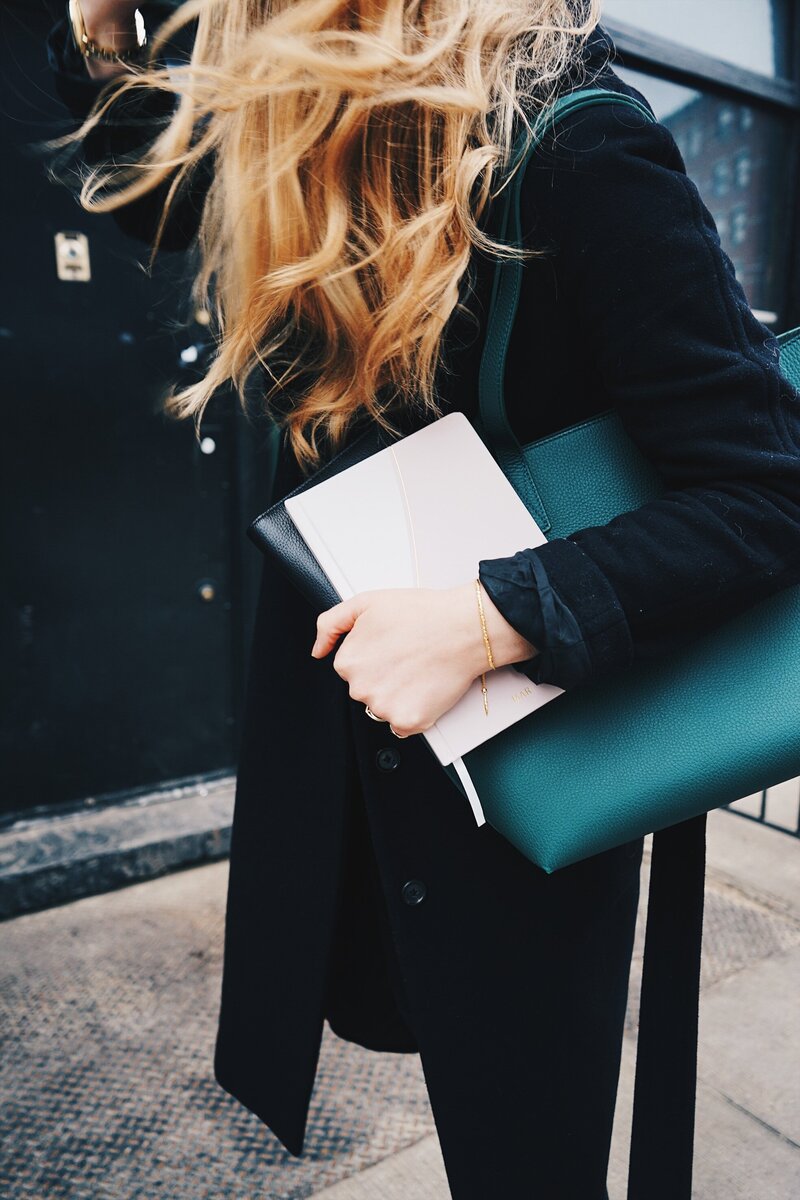 Blonde woman with black coat and emerald green bag