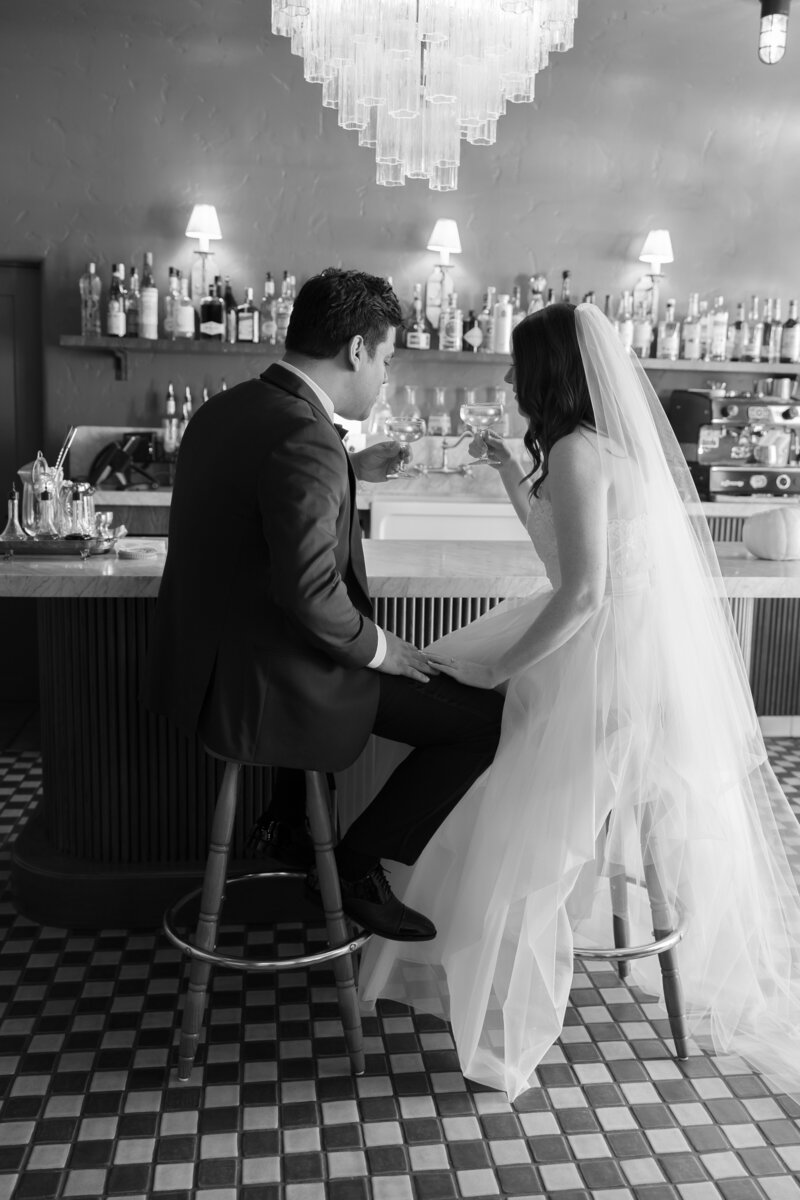 Modern bride and groom smile while sharing cocktails on their wedding day