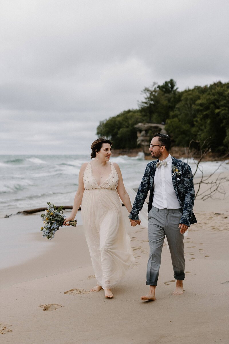 a bride and groom walking along the beach shore holding hands