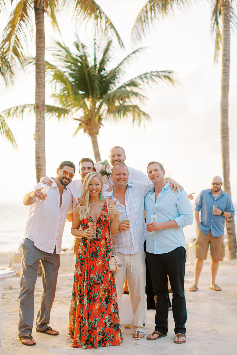 Group of friends celebrating at a beach resort under palm trees during sunset.