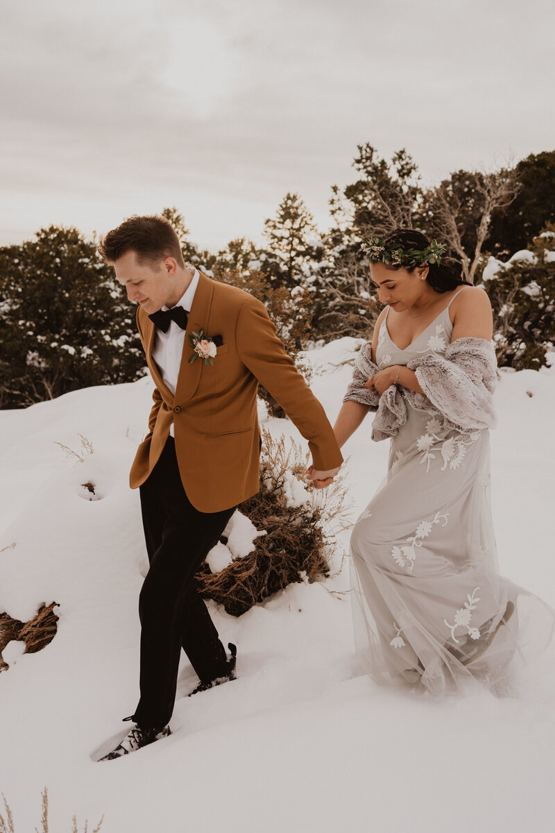 A bride and groom hold hands as they walk through snow.