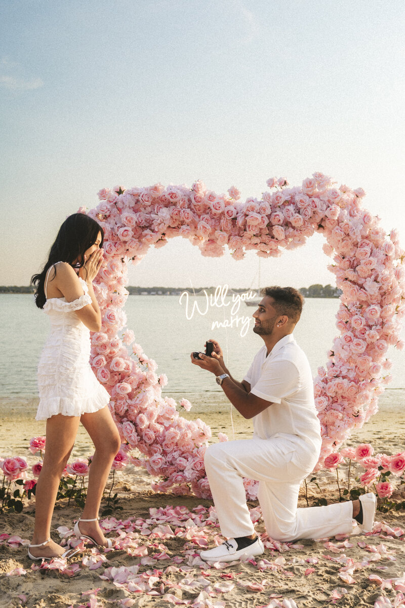 a beach proposal set up with a pink floral heart and a couple styled proposal setup by Yours Truly, a wedding planner and designer in New Jersey.
