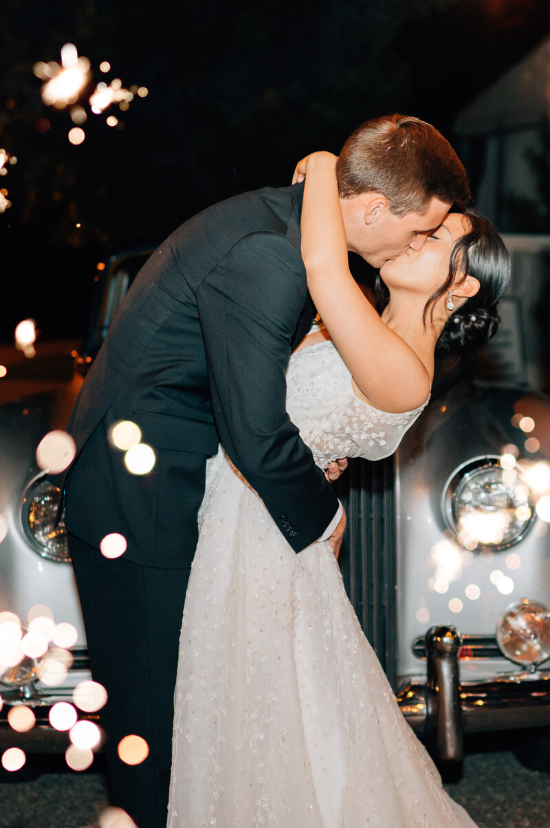 Bride and Groom share a kiss surrounded by sparklers in front of a vintage rolls Royce. Photo by Anna Brace, who specializes in Wedding Photography in Lincoln Nebraska.