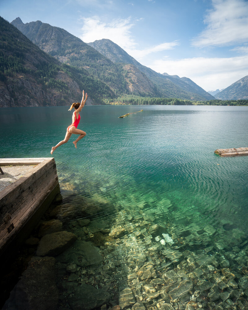 Woman in a red swimsuit jumping into turquoise water surrounded by mountains