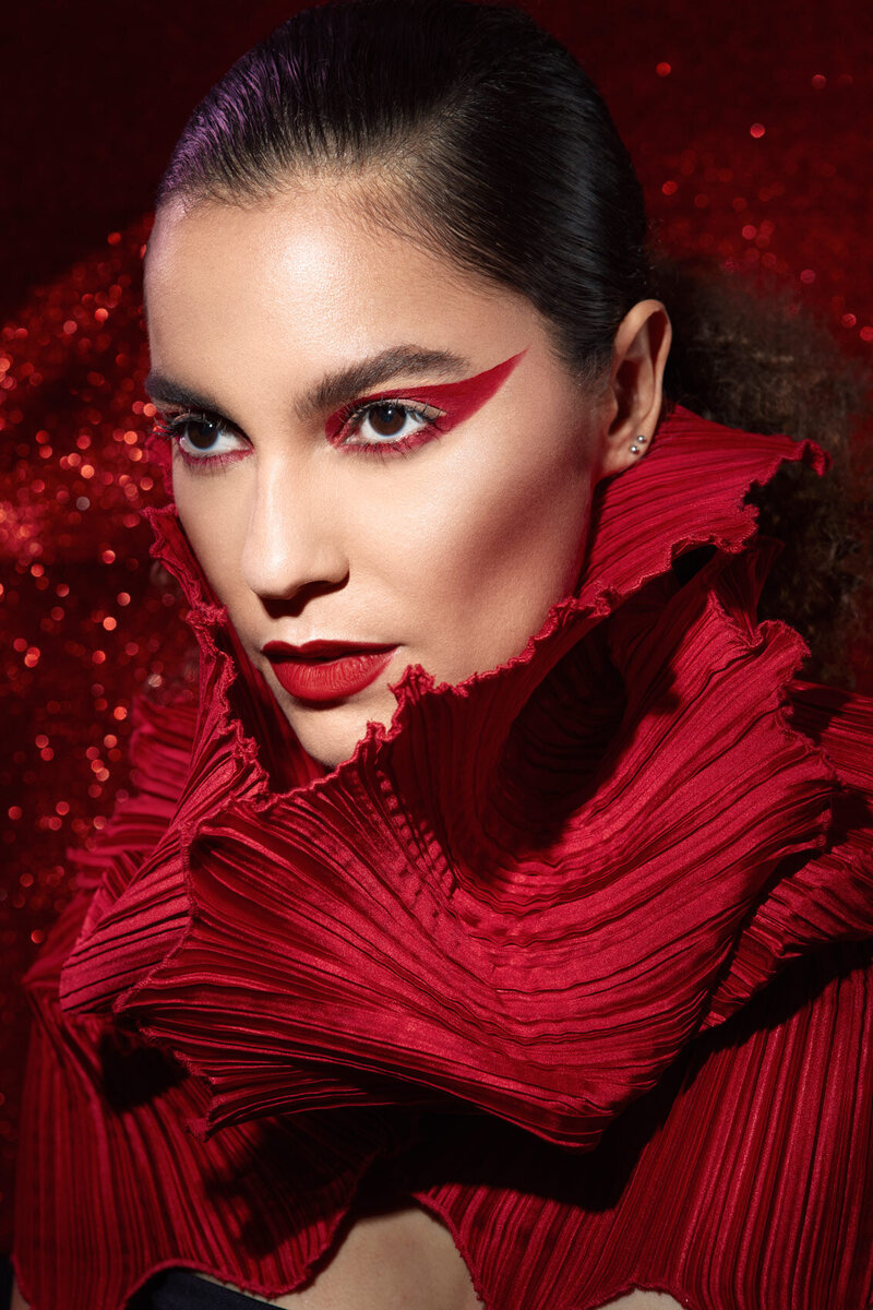 Bold portrait of Artifex in a red textured outfit with striking makeup, captured by Ylva Erevall.
