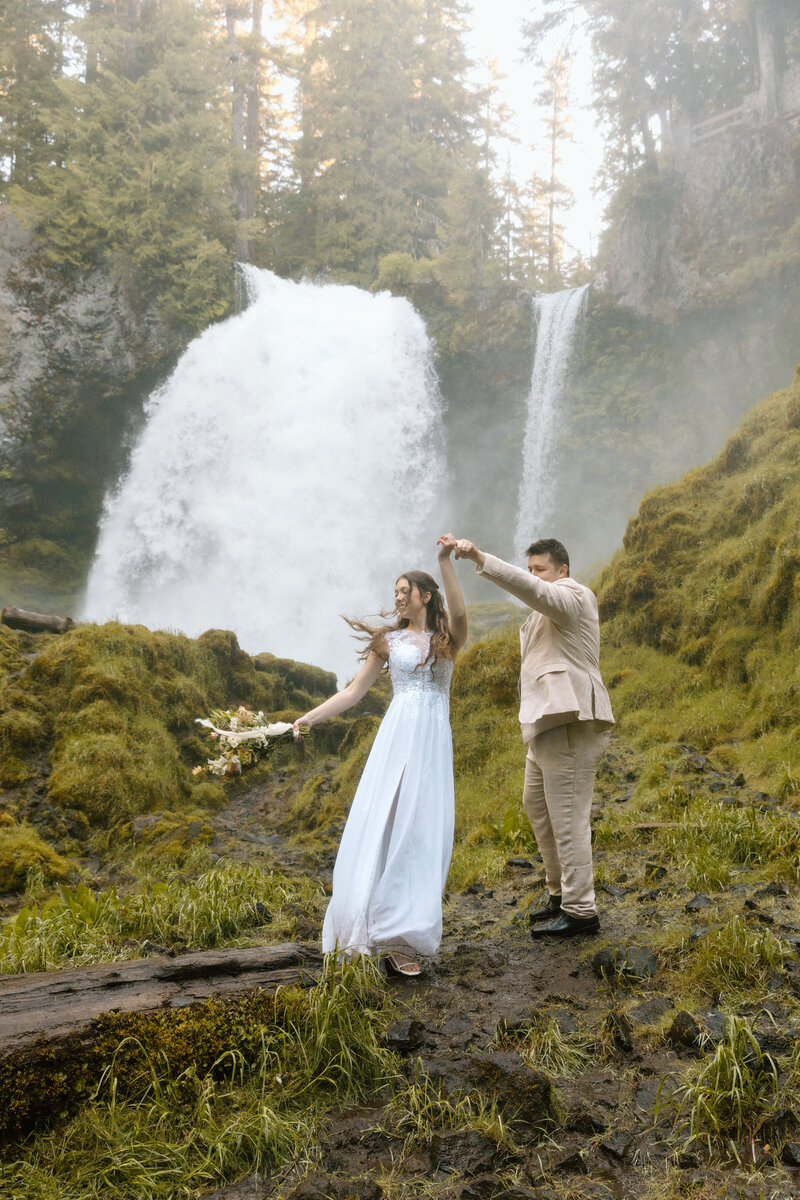 Groom twirling bride at a waterfall in Central Oregon.