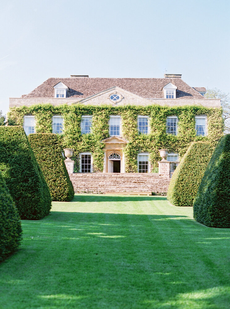 stately home in the Cotswolds with large landscaped trees and covered in ivy