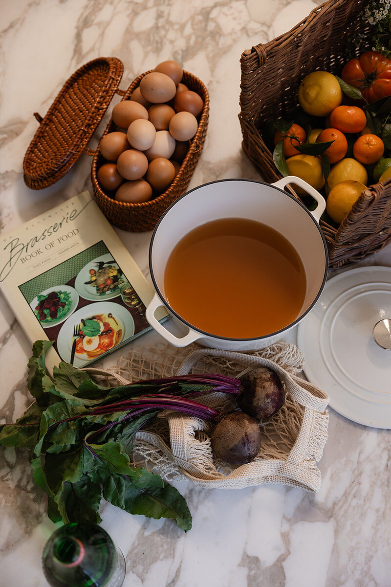 Functional dietician and nutrition kitchen scene with broth, a nutrition book, eggs, and vegetables styled in wicker baskets