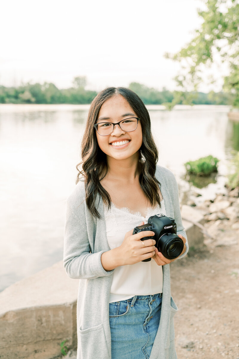 girl next to a river  smiling holding a camera