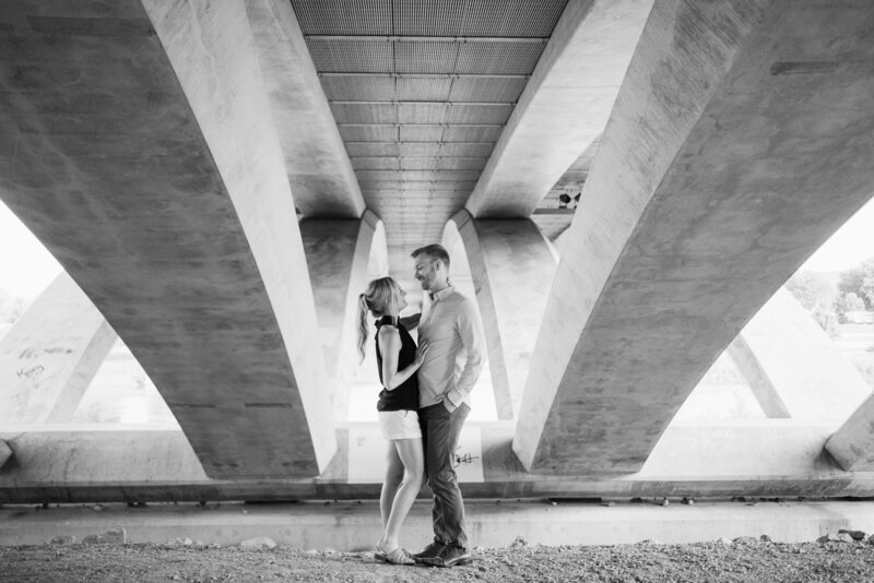 An engaged couple smile at each other under the Main Street Bridge in downtown Columbus