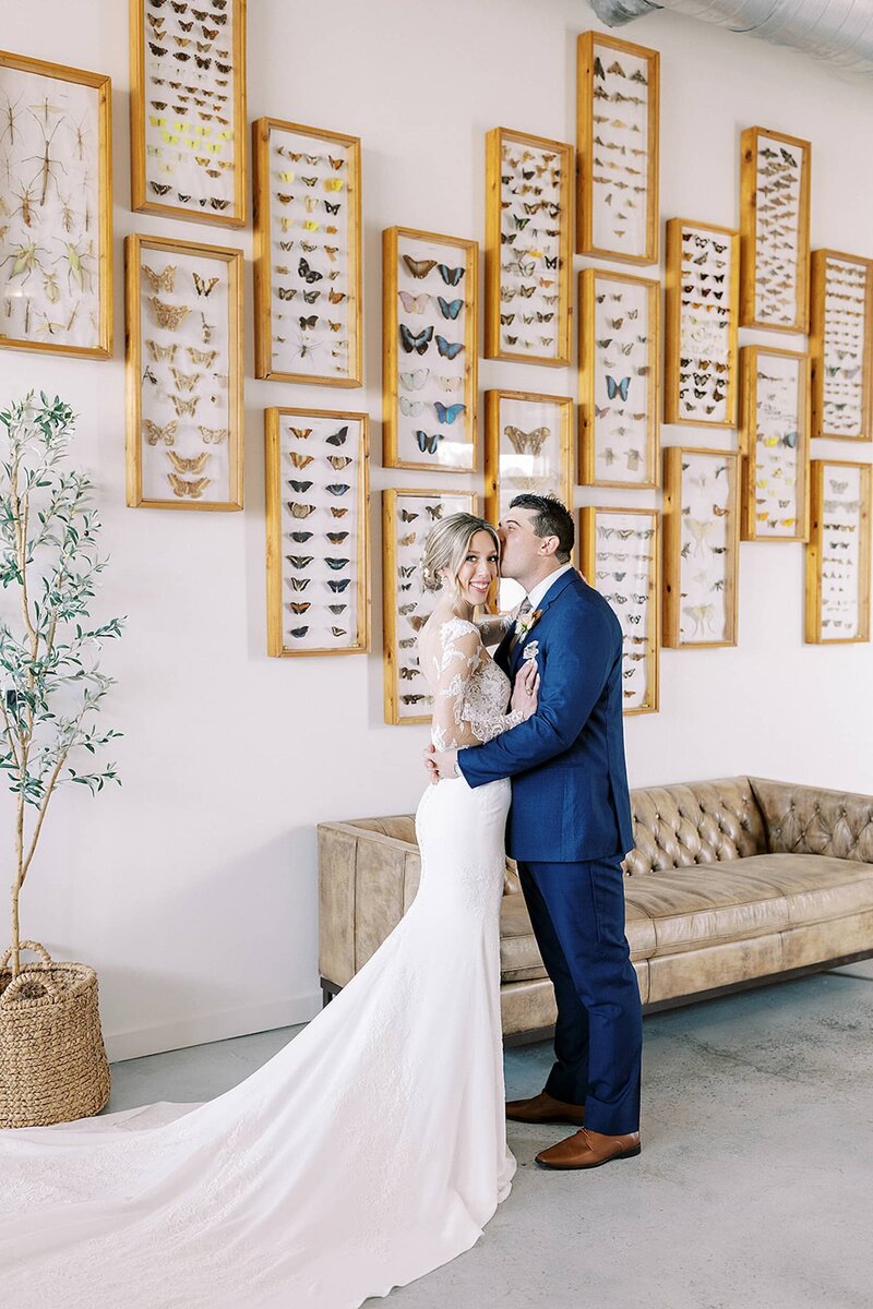 Groom kisses bride in front of butterfly display