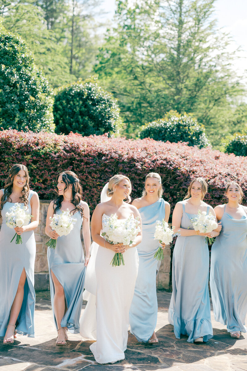 Bride and bridesmaids in blue dresses walk alongside each other laughing back and forth