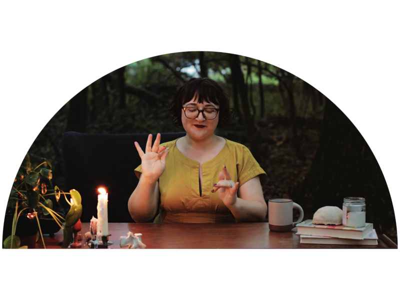 Ash sits at a table in the forest at sunset with a lit candle practicing energy work