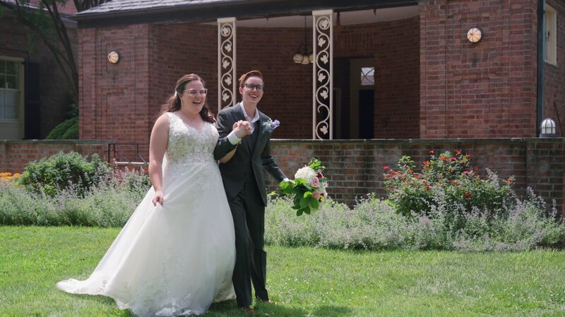 Kassie & Juliette  hold hands as they celebrate their union walking in a field of grass at newton white mansion happily ever after.