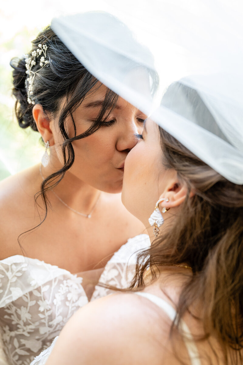 lesbian brides kissing with one of the bride's veils over their heads