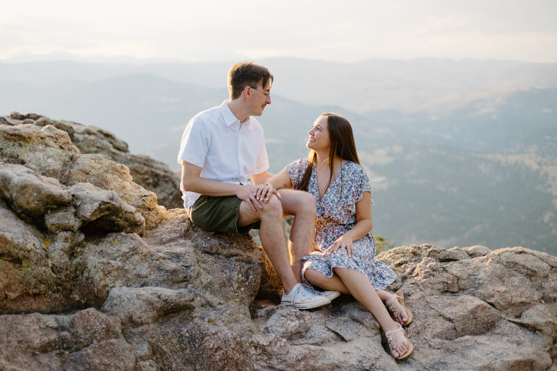 At Lost Gulch Overlook in Boulder, Colorado, an engaged couple shares a joyful moment, smiling at each other with the stunning landscape in the background.
