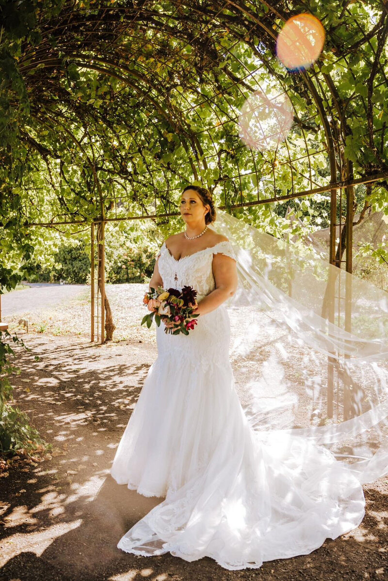 bride wearing her custom pearl bridal veil while standing under an arbor