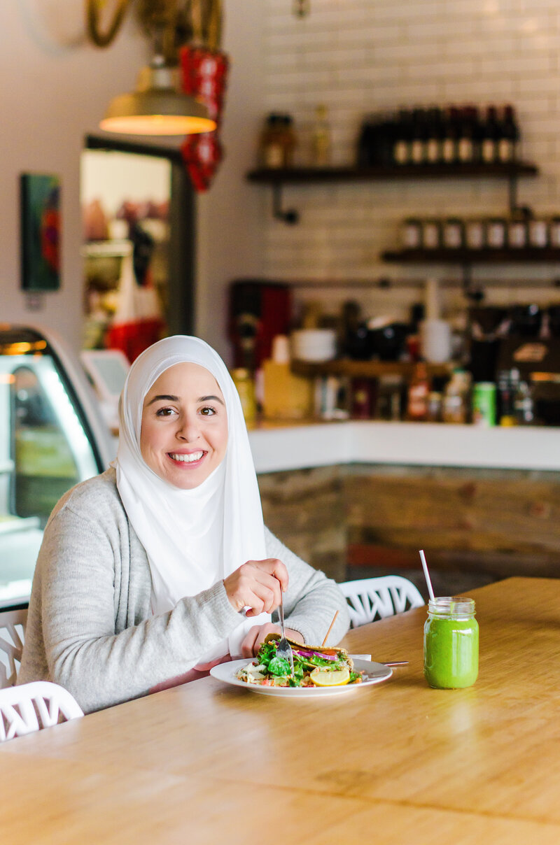 Fitness hijabi coach Hanan posing with a smile as she is eating a healthy salad meal with a side of a green smoothie in a mason jar