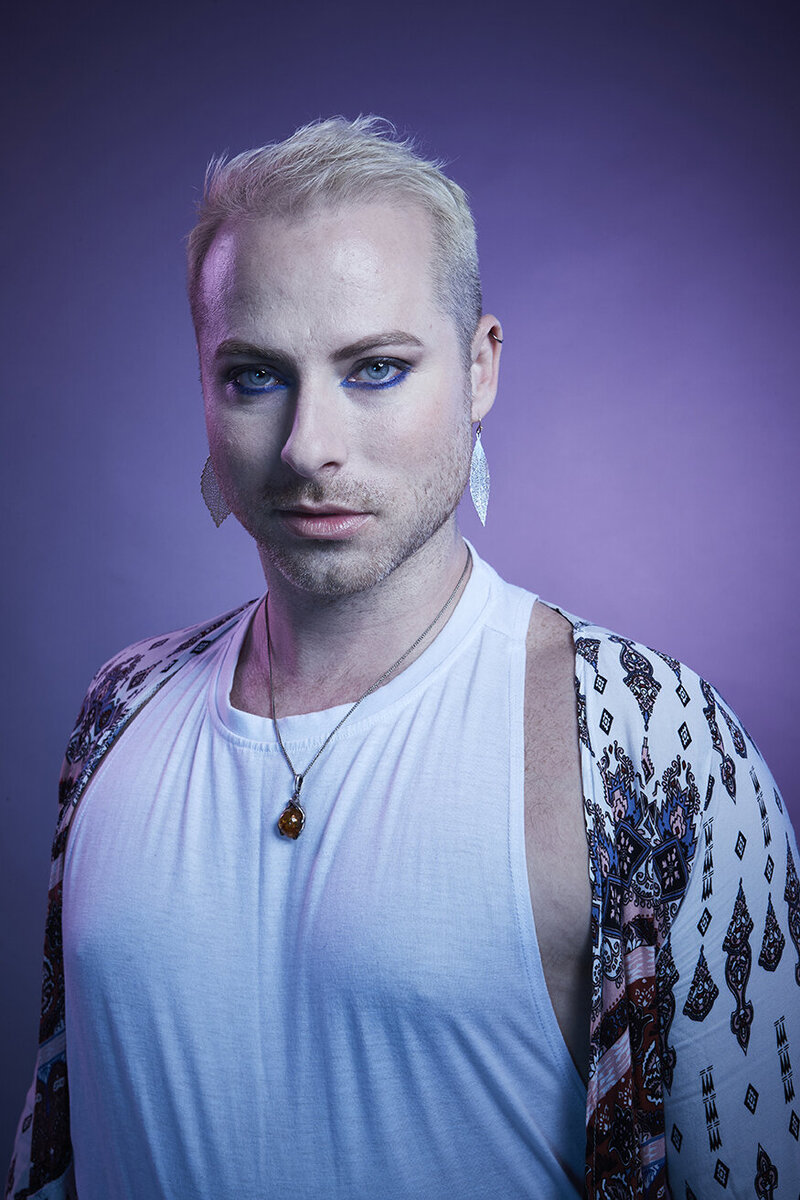 Close-up portrait of Dain August in a white and black patterned outfit, with a confident and intense gaze, photographed by Ylva Erevall.