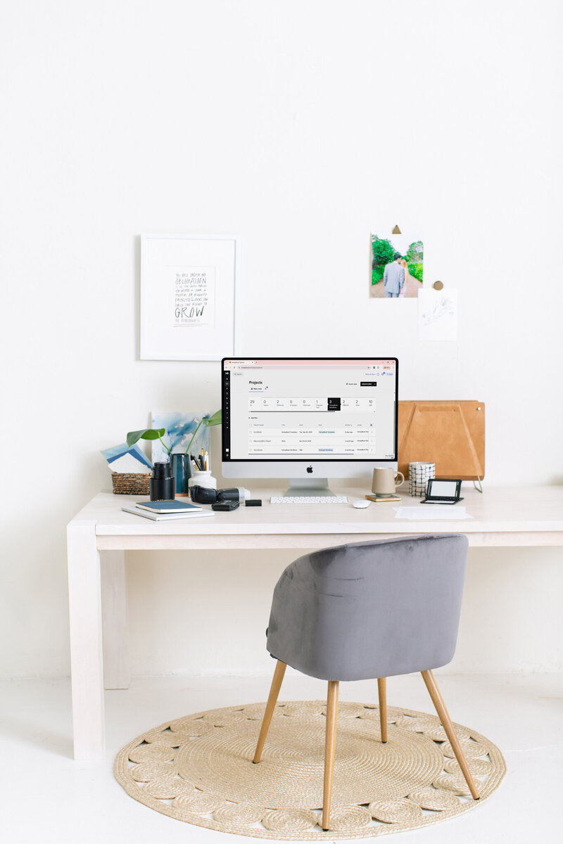 Minimal white desk workspace with an iMac computer, notebooks, plant, and neutral decor, representing organized workflows and simplified systems for wedding photographers.