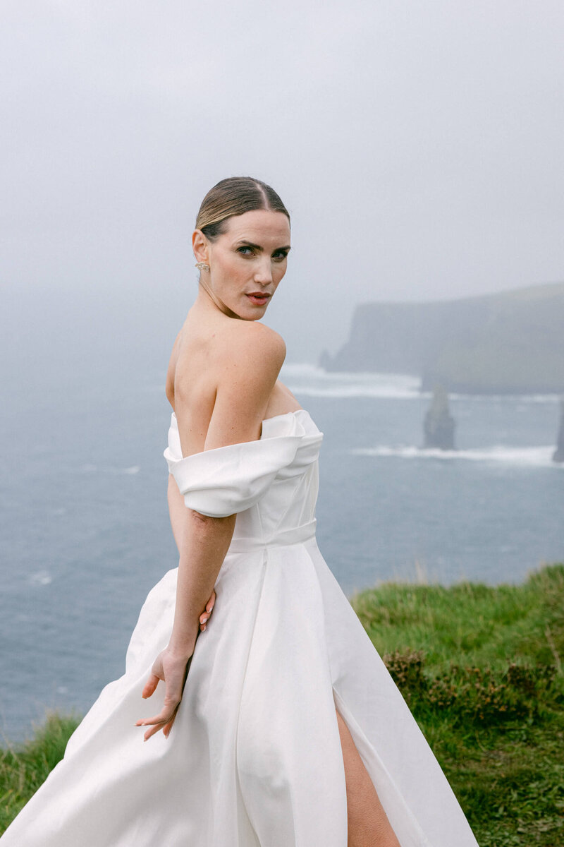 Bride posing for her portrait at the top of the cliffs of Moher with the ocean in the background