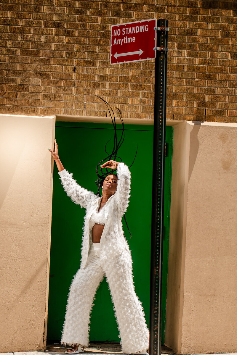 Andrea Pitter-Campbell, renowned fashion designer, stuns in a white three-piece Pandora Bridal set while tossing her braids in New York City. A powerful lifestyle portrait highlighting her elegance and spirit.