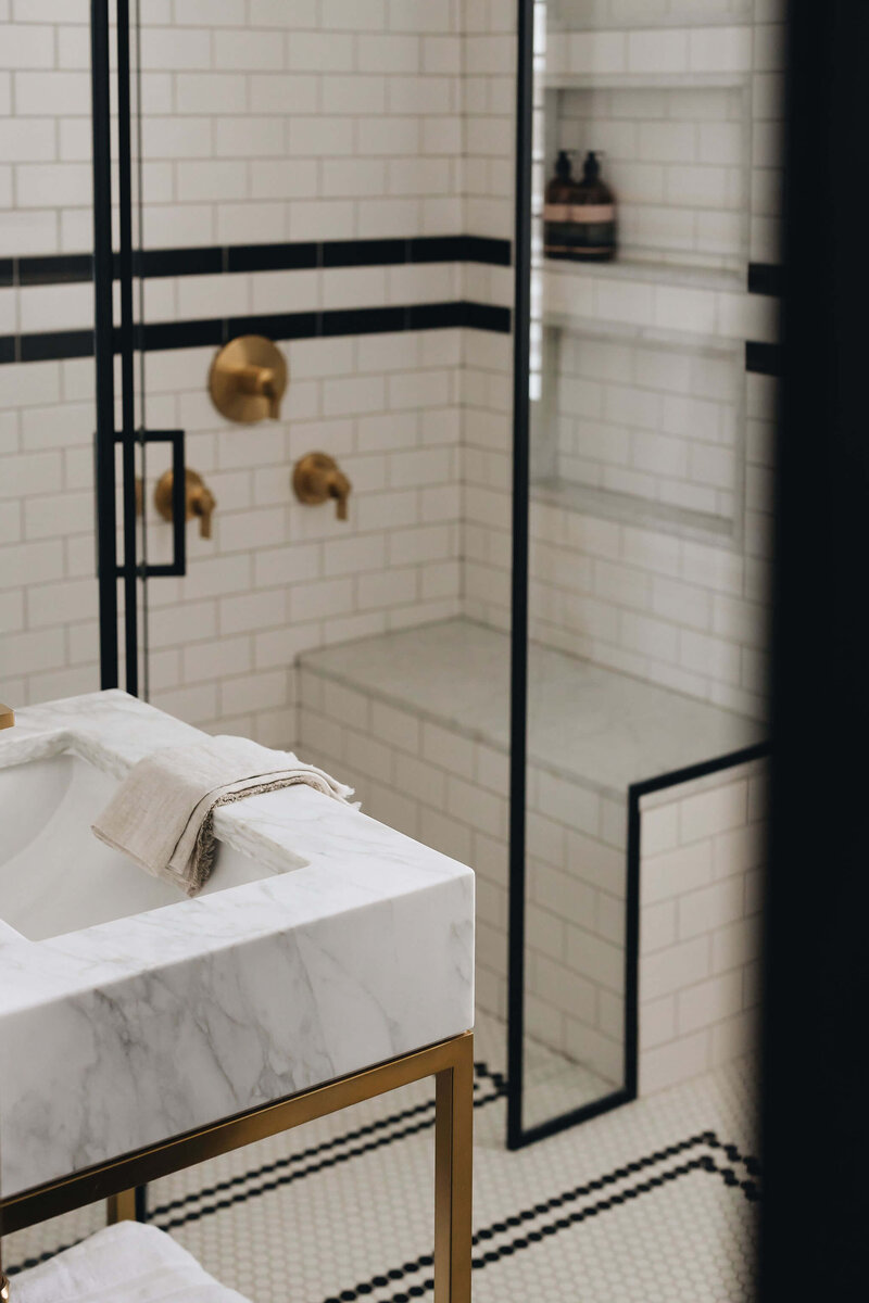 Marble bathroom sink in front of hexagonal tiles with brass hardware