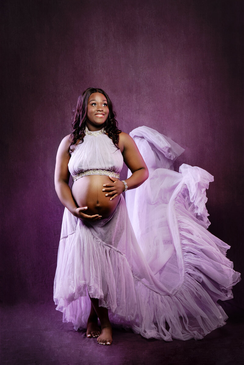 st-louis-maternity-photographer-expecting-mom-in-two-piece-purple-tulle-dress-that-has movement-on-purple-backdrop