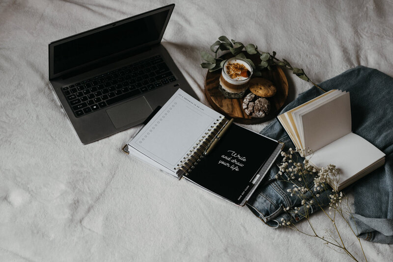 Laptop and open planner on a bed with a tray of coffee and cookies