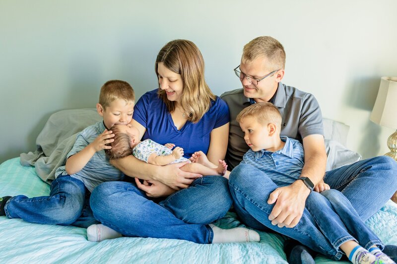 Family sitting together on a bed looking at newborn. 