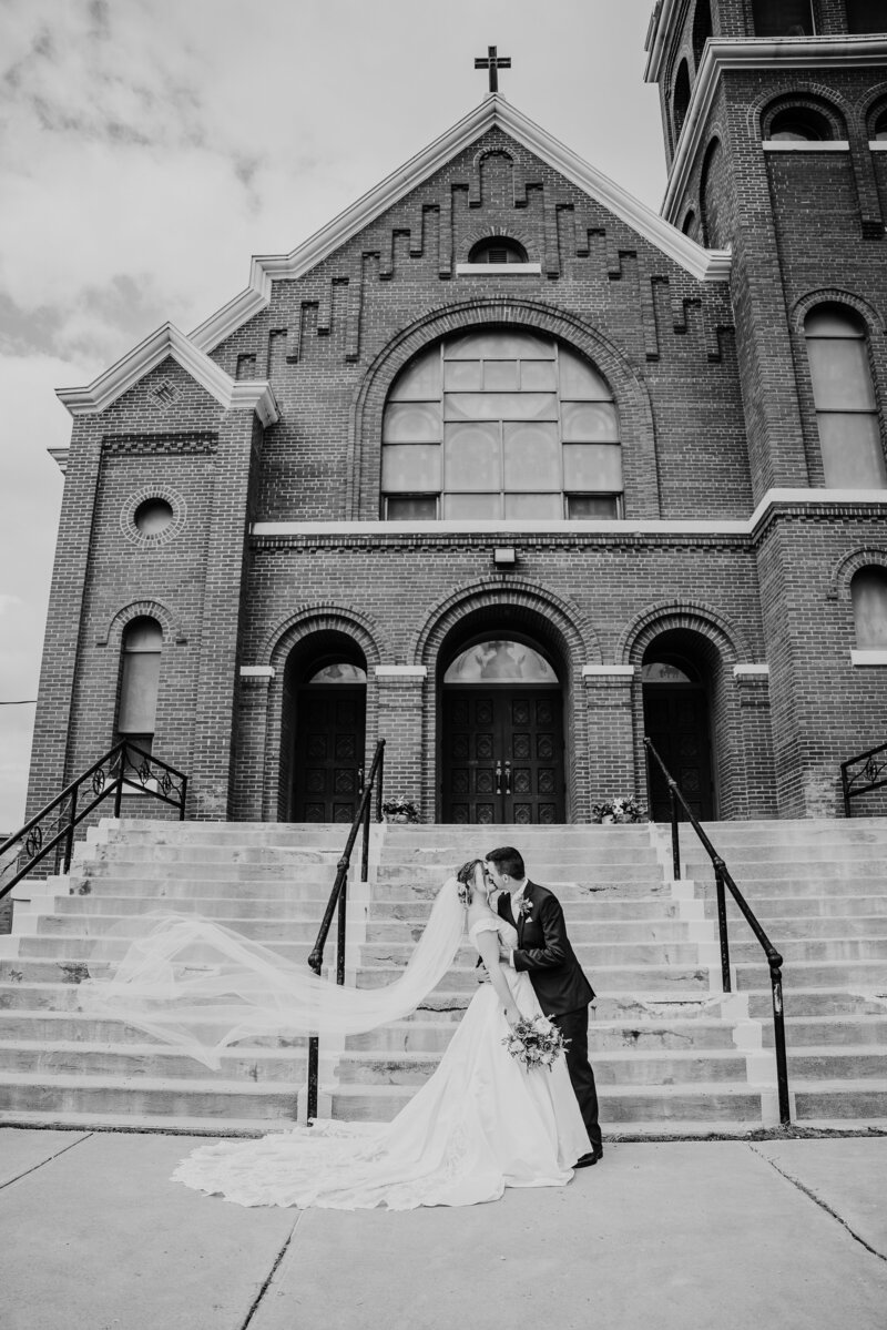 A couple poses in front of their church in Eau Claire WI as the bride's veil blows in the wind.