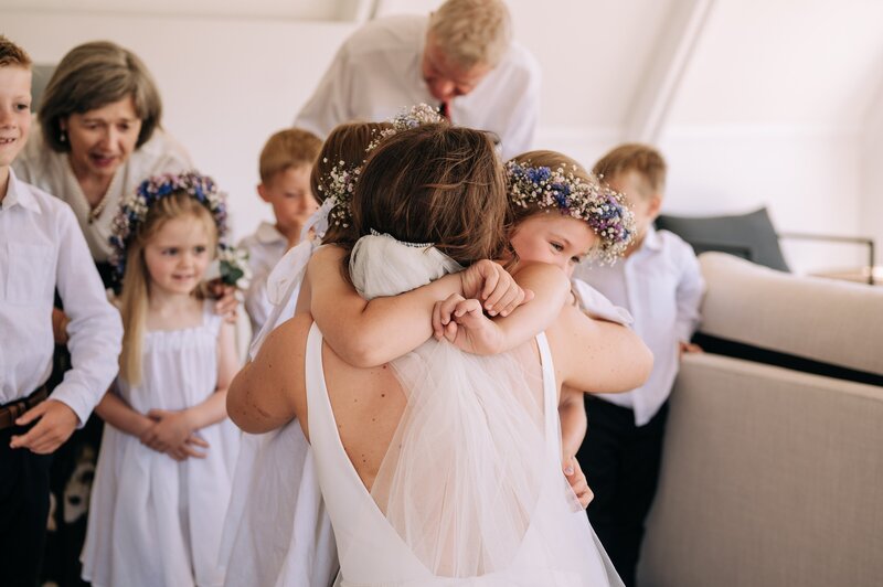bride hugs children in white with flower crowns at akaroa wedding airbnb while getting ready