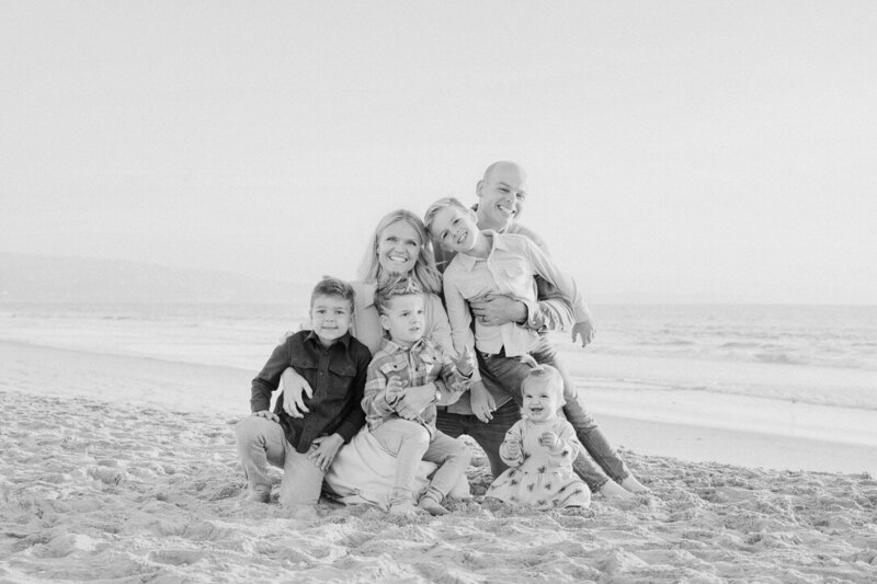 Emily Collins with her husband and four children smiling and sitting together on the beach in a black and white photo