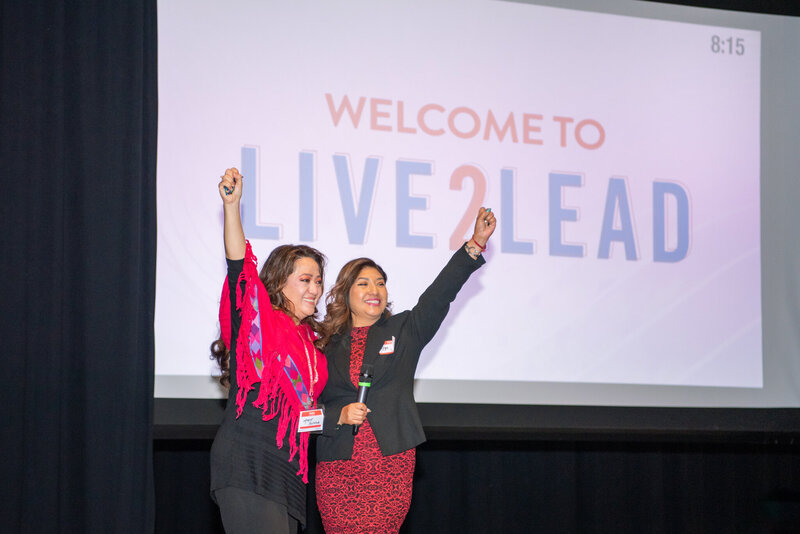 Two women with their hands up excited for a Live2Lead conference.