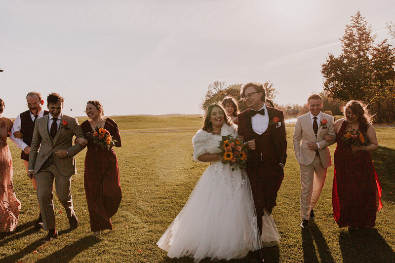 Bride and groom holding hands with wedding party behind them walking candidly 