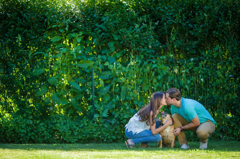 Couple sharing a romantic kiss while lovingly holding their puggle, showcasing their bond during an engagement photography session with dogs.