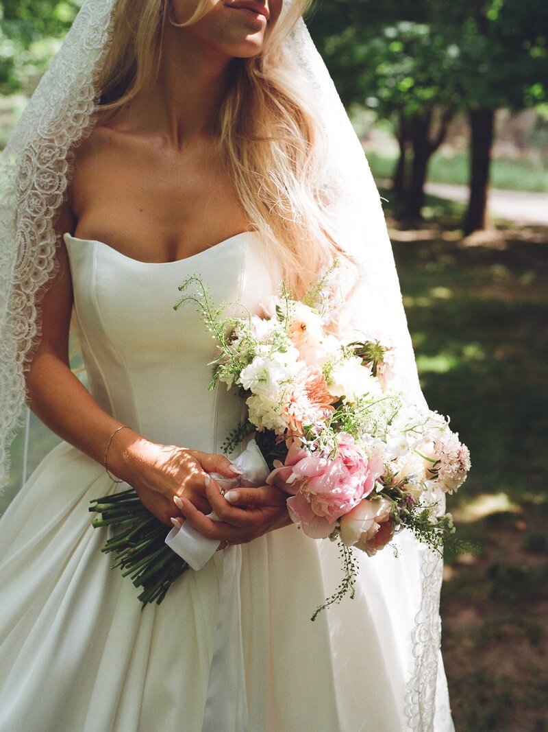 Bride in a strapless gown holding a lush pastel wedding bouquet with lace veil detail, captured by a Washington state photographer.