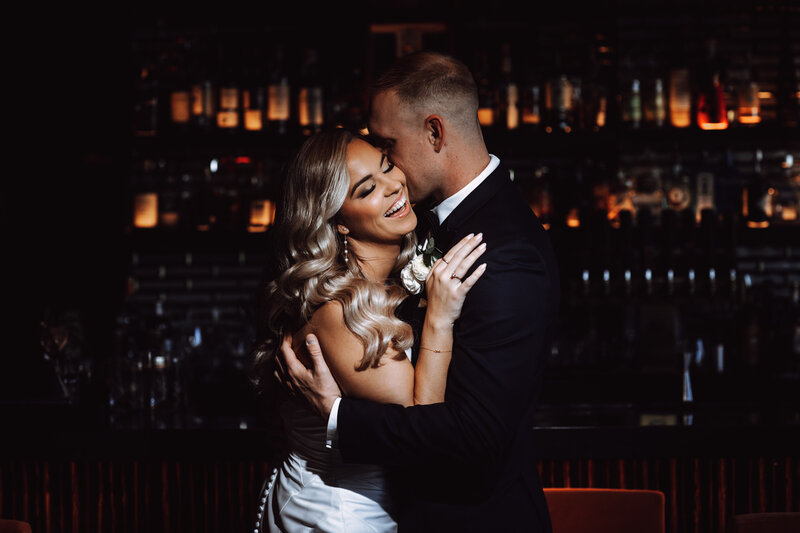 A bride and groom embrace inside a dark wedding reception hall