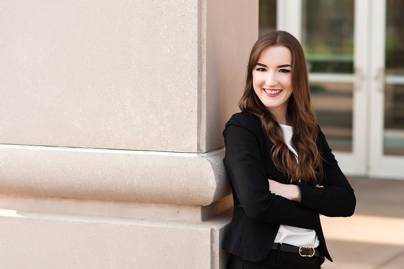Boss babe rocking a power pose in her fitted suit, arms crossed leaning against wall and smiling boldly at the camera