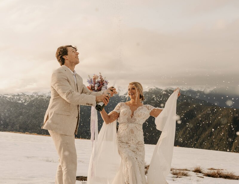 just married couple celebrate popping champagne on a mountaintop at sunrise after banff elopement with danielle boulger photography