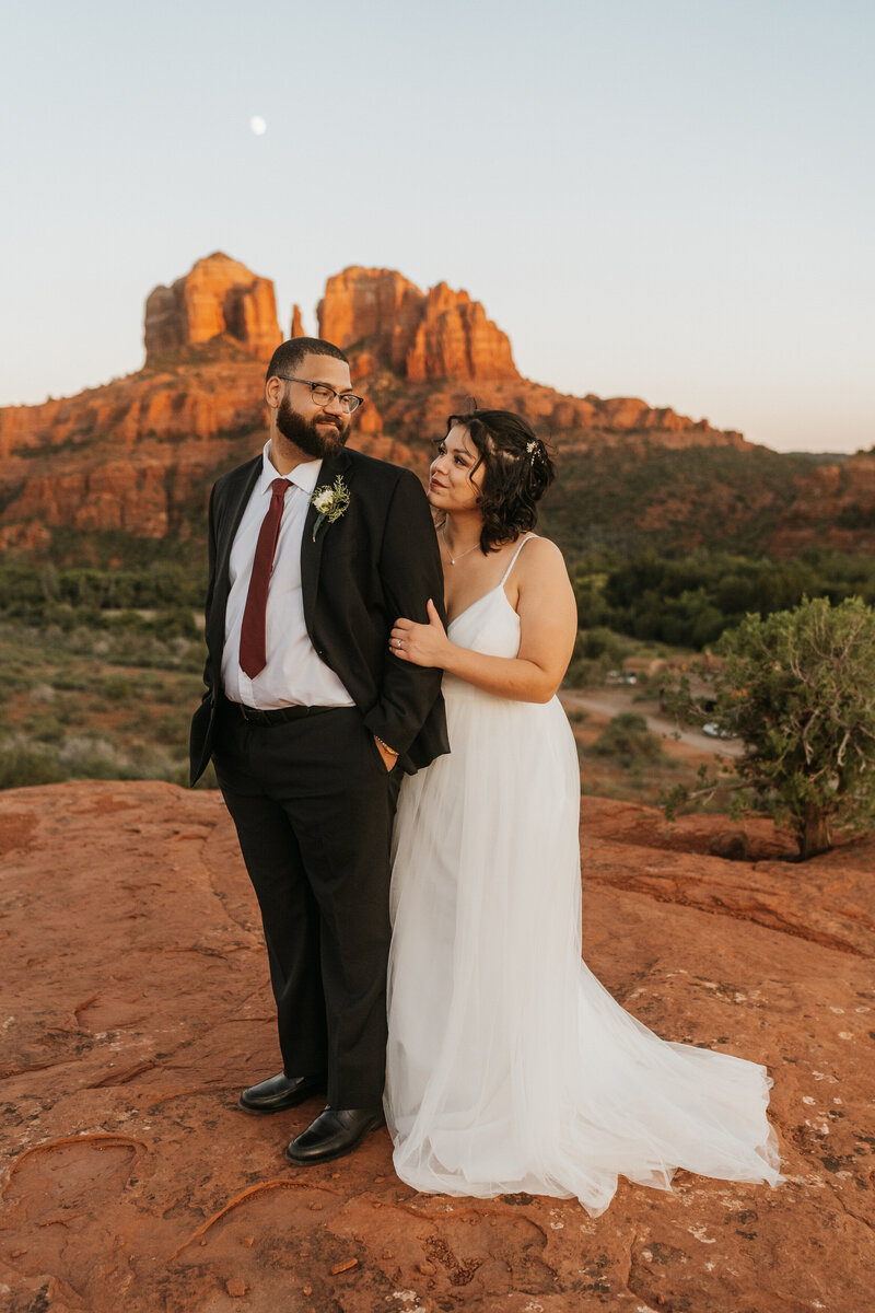 A person standing behind their partner holding their arm as they smile at each other