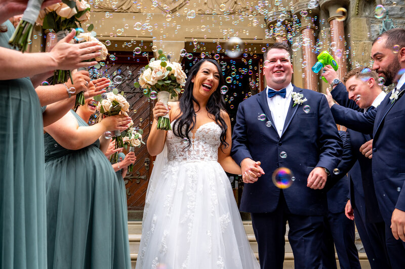 A bride and groom exiting a church through bubbles after getting married.